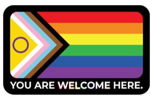 Progress Pride Flag: Regenbogenflagge mit eingearbeiteter  Intersex*- und Transgender-Flagge und den Farben der POC-Community.  Darunter der Schriftzug: You are welcome here.